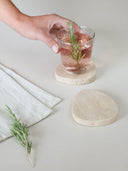 Twee beige natuursteen travertijn onderzetters van het merk Leeff met een diameter van 10 cm.