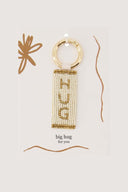 Zusss sleutelhanger hug in metaal en papier met witte en okergele kralen en een goudkleurige ring.
